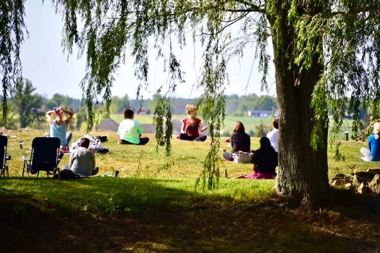Megan Bennett teaching outdoor yoga class under a willow tree at Peace Of Heart Yoga